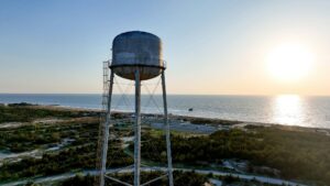Vintage water tower on top of a rocky hill, overlooking a tranquil blue ocean